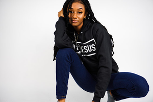 girl squatting with a black #Jesus hoodie on she has a hand rested on her chin